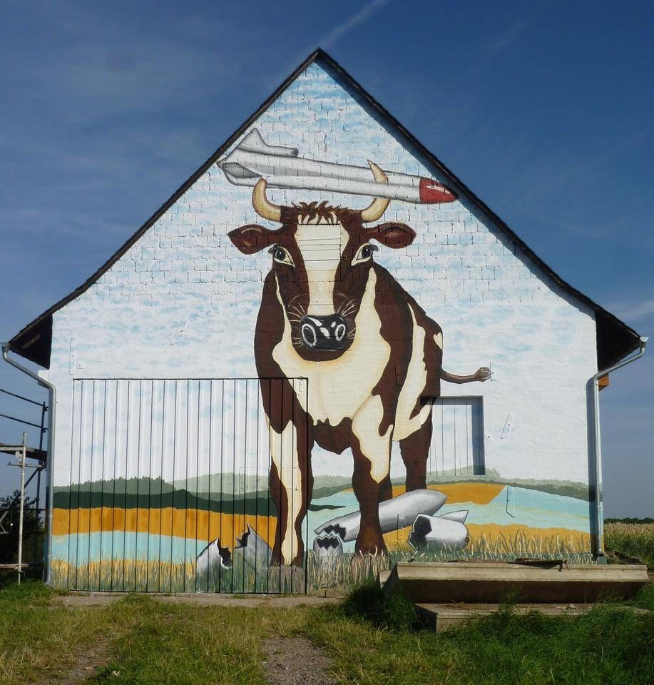 Giebel einer Scheune mit dem Wandbild einer Kuh, die eine Rakete auf die Hörner nimmt